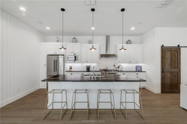 kitchen featuring white cabinets, a barn door, stainless steel appliances, and an island with sink