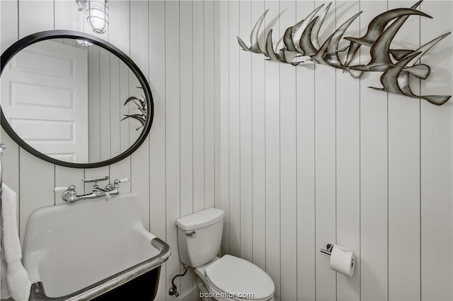 bathroom featuring wood walls, sink, and toilet