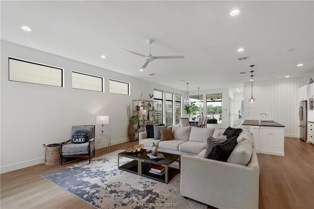 living room featuring ceiling fan, sink, and light wood-type flooring