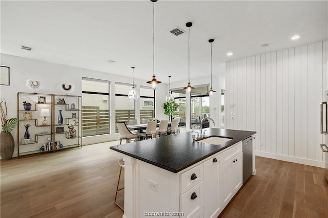 kitchen featuring a kitchen island with sink, sink, dishwasher, white cabinets, and hardwood / wood-style floors