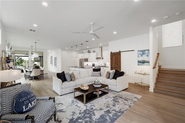 living room with a barn door, ceiling fan, and light wood-type flooring