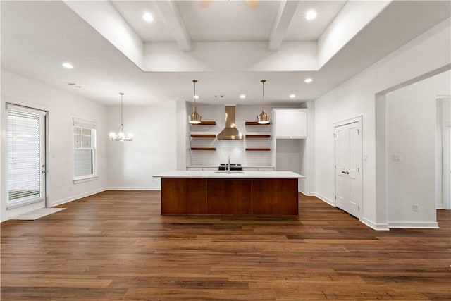 kitchen featuring sink, wall chimney exhaust hood, beamed ceiling, an island with sink, and pendant lighting