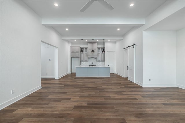 unfurnished living room featuring beam ceiling, a barn door, dark hardwood / wood-style flooring, and ceiling fan