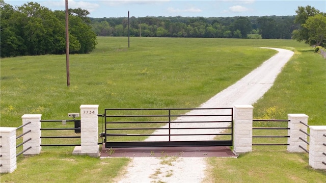 view of gate featuring fence, a lawn, and a rural view