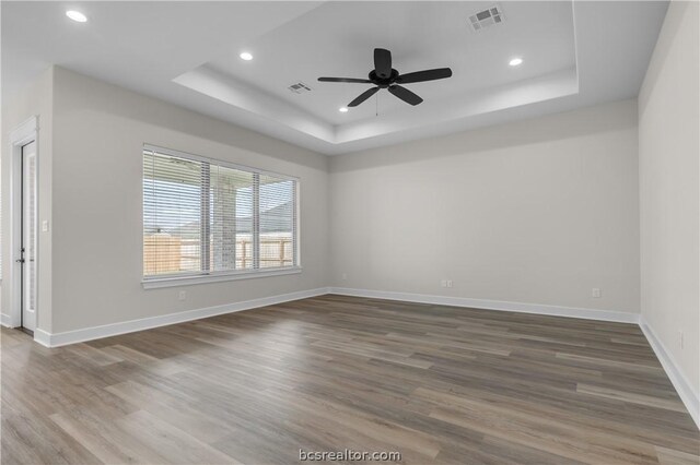 unfurnished room featuring a raised ceiling, ceiling fan, and hardwood / wood-style flooring