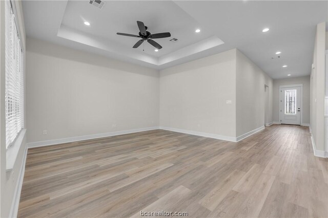 spare room with light wood-type flooring, a tray ceiling, and ceiling fan