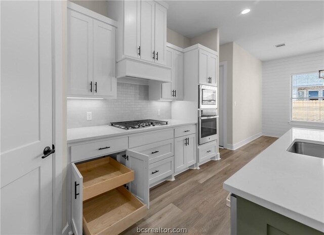 kitchen with appliances with stainless steel finishes, light wood-type flooring, tasteful backsplash, and white cabinetry