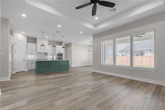 kitchen with a center island with sink, light hardwood / wood-style flooring, hanging light fixtures, white cabinetry, and stainless steel microwave