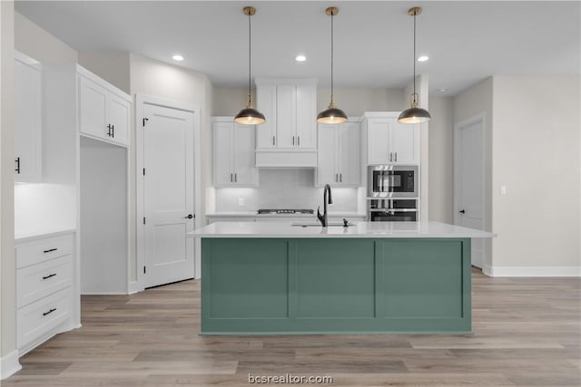 kitchen with a center island with sink, white cabinets, sink, decorative light fixtures, and stainless steel appliances