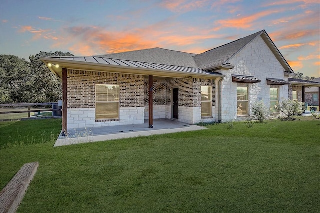 back house at dusk with a patio area and a lawn