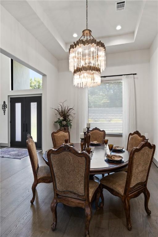 dining space featuring wood-type flooring, a healthy amount of sunlight, a tray ceiling, and a notable chandelier