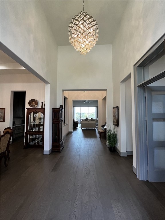 hall with a towering ceiling, a notable chandelier, and dark hardwood / wood-style floors