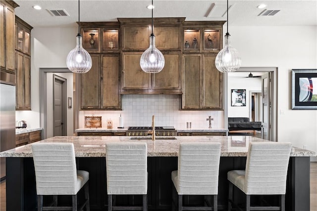 kitchen featuring pendant lighting, a kitchen island with sink, light stone counters, and decorative backsplash