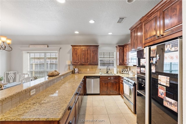 kitchen featuring sink, stainless steel appliances, an inviting chandelier, light stone counters, and light tile patterned floors