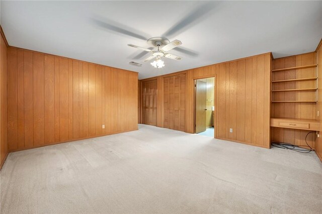 unfurnished bedroom with wooden walls, carpet, and a ceiling fan