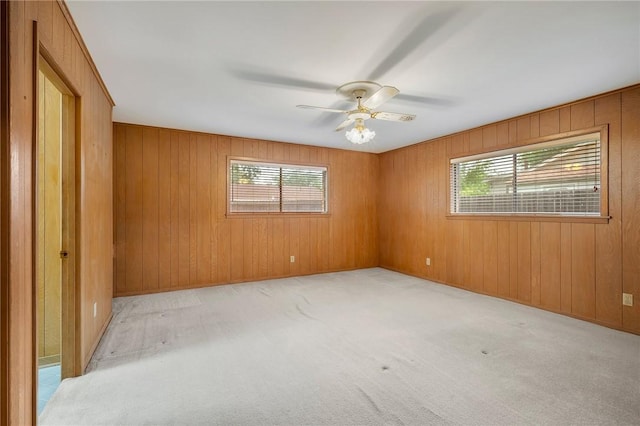 empty room with plenty of natural light, a ceiling fan, wood walls, and carpet floors