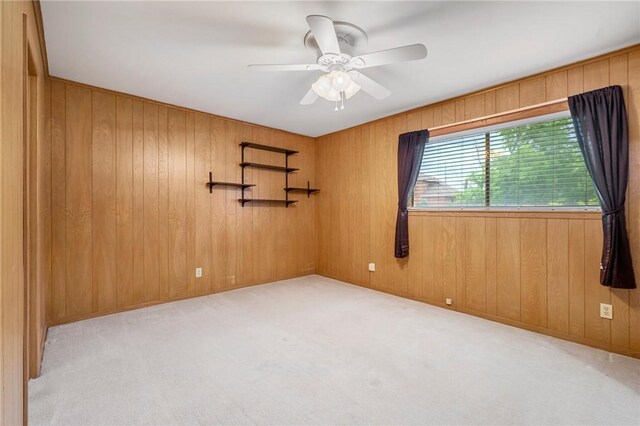 empty room with carpet flooring, a ceiling fan, and wooden walls