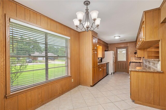 kitchen with plenty of natural light, a chandelier, light tile patterned floors, freestanding refrigerator, and wooden walls
