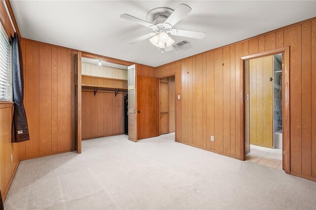 unfurnished bedroom featuring carpet flooring, wood walls, a closet, and ceiling fan