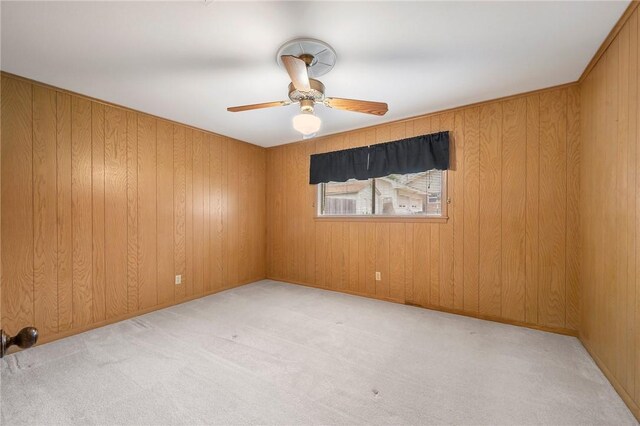 spare room with carpet floors, a ceiling fan, and wood walls