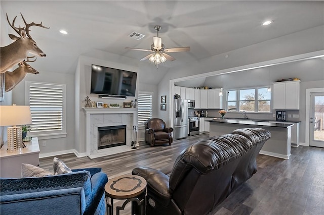 living room featuring dark wood-type flooring, vaulted ceiling, visible vents, and a fireplace