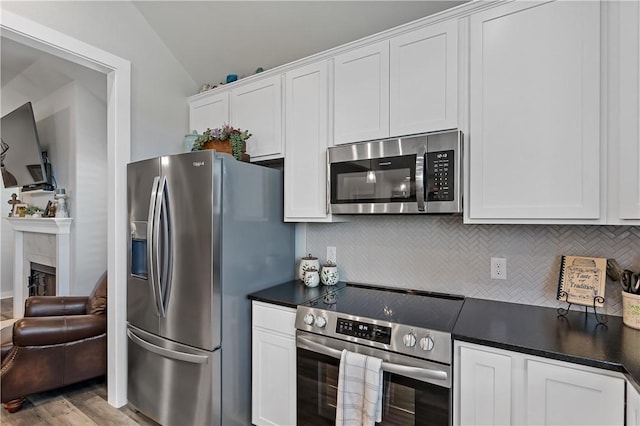 kitchen featuring stainless steel appliances, dark countertops, lofted ceiling, backsplash, and white cabinets