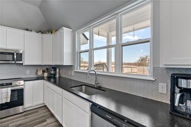 kitchen featuring dark countertops, vaulted ceiling, stainless steel appliances, and a sink