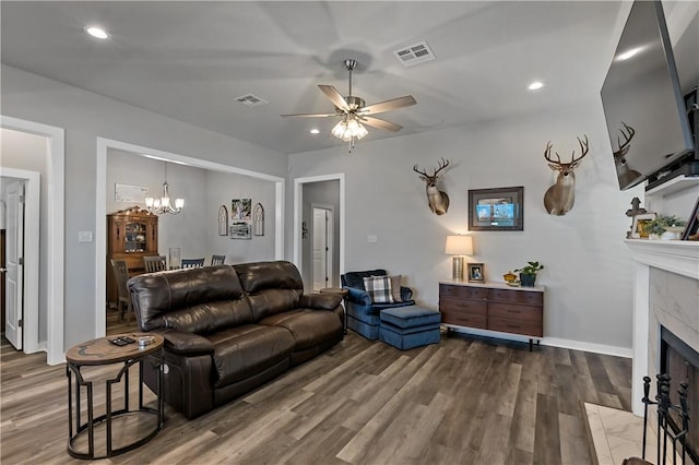 living room featuring ceiling fan with notable chandelier, visible vents, a tiled fireplace, and wood finished floors