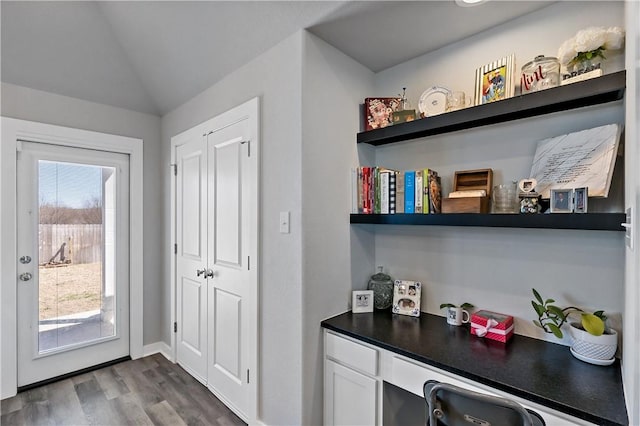 interior space featuring lofted ceiling, built in desk, dark wood-style floors, and baseboards