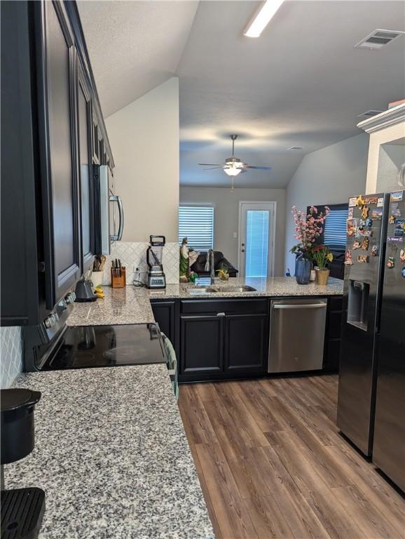 kitchen featuring sink, stainless steel appliances, light stone countertops, dark hardwood / wood-style flooring, and vaulted ceiling