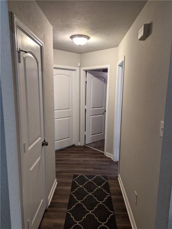 hall with a textured ceiling and dark hardwood / wood-style flooring