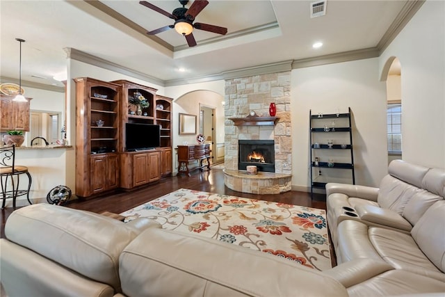 living room with visible vents, dark wood-type flooring, arched walkways, a stone fireplace, and ceiling fan