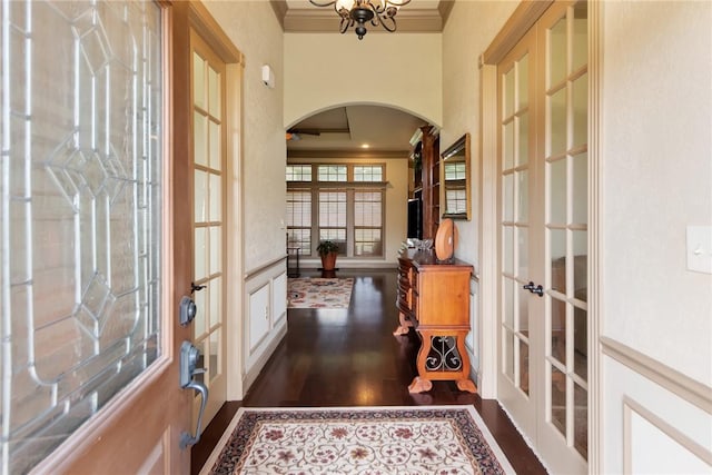 doorway with dark wood finished floors, ornamental molding, french doors, an inviting chandelier, and arched walkways