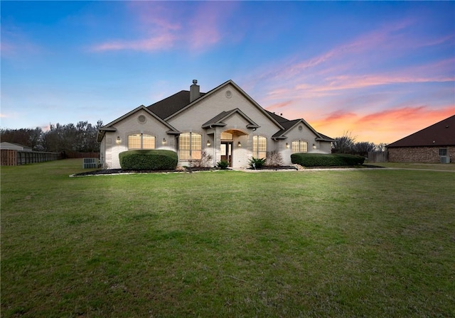 french provincial home with a front lawn, fence, brick siding, and a chimney