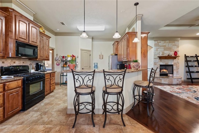 kitchen featuring tasteful backsplash, crown molding, a stone fireplace, a kitchen breakfast bar, and black appliances