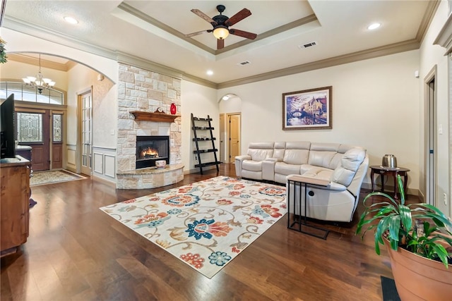 living room featuring visible vents, dark wood-type flooring, ceiling fan with notable chandelier, a stone fireplace, and a raised ceiling