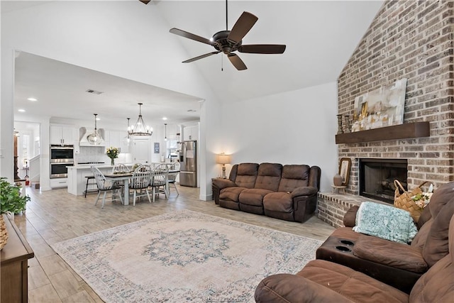 living room featuring a fireplace, light wood-type flooring, high vaulted ceiling, and ceiling fan