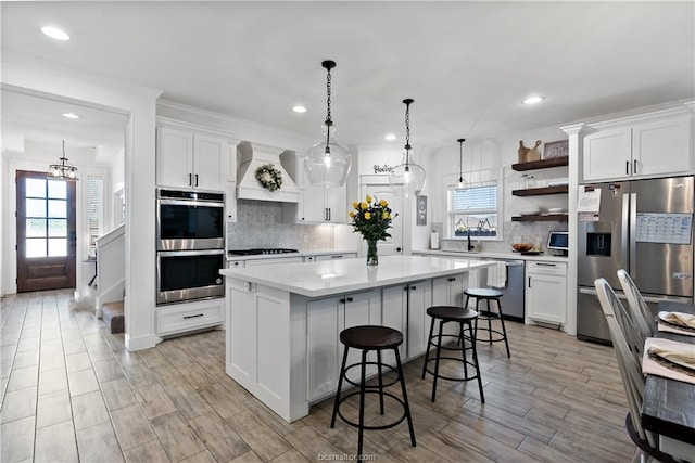 kitchen featuring premium range hood, white cabinets, decorative light fixtures, a kitchen island, and stainless steel appliances