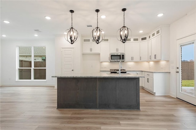 kitchen with a center island with sink, light stone counters, white cabinetry, and light hardwood / wood-style flooring