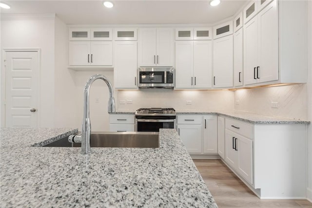 kitchen featuring sink, light wood-type flooring, light stone countertops, white cabinetry, and stainless steel appliances