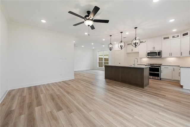 kitchen featuring appliances with stainless steel finishes, light wood-type flooring, white cabinetry, hanging light fixtures, and an island with sink