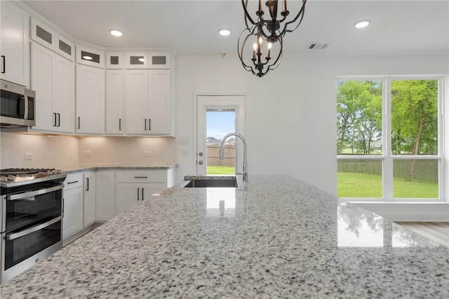 kitchen with white cabinetry, hanging light fixtures, stainless steel appliances, light stone counters, and a notable chandelier