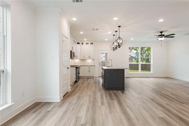 kitchen with white cabinets, ceiling fan with notable chandelier, a center island with sink, light hardwood / wood-style flooring, and appliances with stainless steel finishes