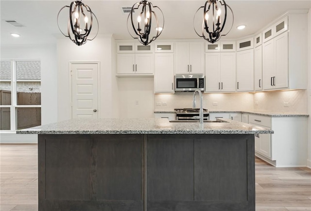 kitchen featuring light stone countertops, light hardwood / wood-style flooring, white cabinetry, hanging light fixtures, and an island with sink