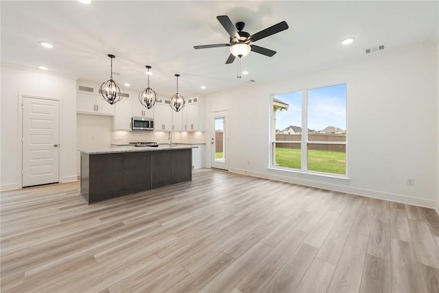 kitchen with white cabinetry, a kitchen island with sink, decorative light fixtures, and light wood-type flooring