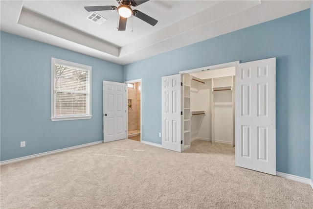 unfurnished bedroom featuring ceiling fan, a raised ceiling, light carpet, a walk in closet, and a closet