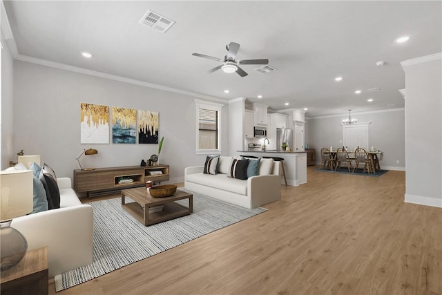 living room with crown molding, ceiling fan with notable chandelier, and light hardwood / wood-style flooring