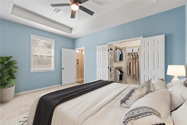 carpeted bedroom with ceiling fan, connected bathroom, a tray ceiling, a spacious closet, and a closet