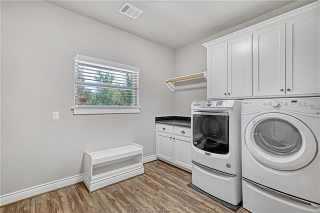 washroom with light hardwood / wood-style floors, cabinets, and washing machine and clothes dryer