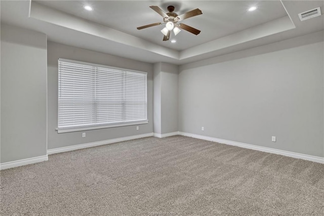 empty room featuring carpet, a raised ceiling, and ceiling fan